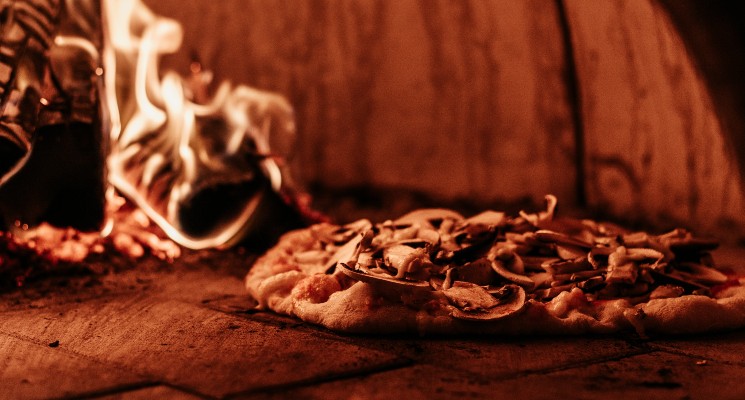 image of pizza in front of burning pizza oven fire