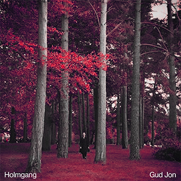 A man in a long black coat walks through a forest of trees with pink leaves